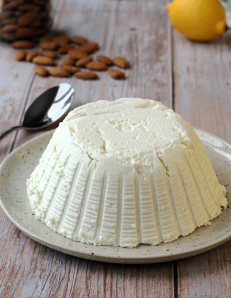 Dairy free ricotta cheese made with almonds on plate with almonds and lemon behind it.