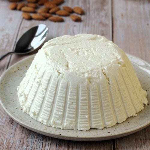 Dairy free ricotta cheese on plate with spoon next to it and almonds.