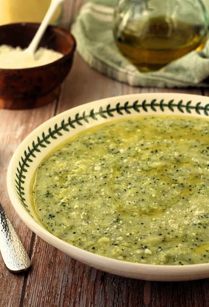 Sicilian polenta with broccoli in round palte with bowl of cheese and olive oil behind it.