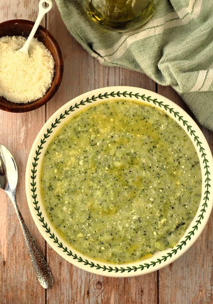 Bowl of polenta with broccoli with bowl of cheese on side and spoon.
