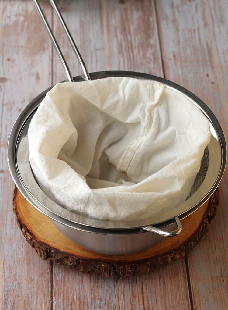 Nut milk bag over sieve placed over bowl.