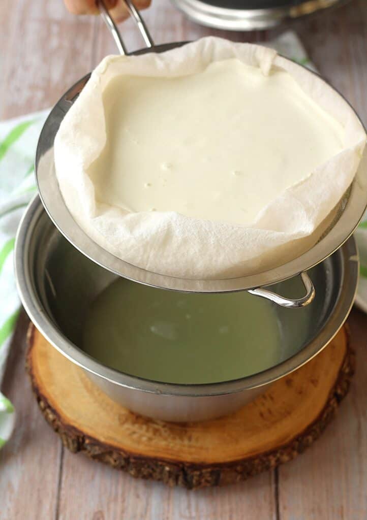 Almond milk ricotta in sieve draining whey in bowl underneath.