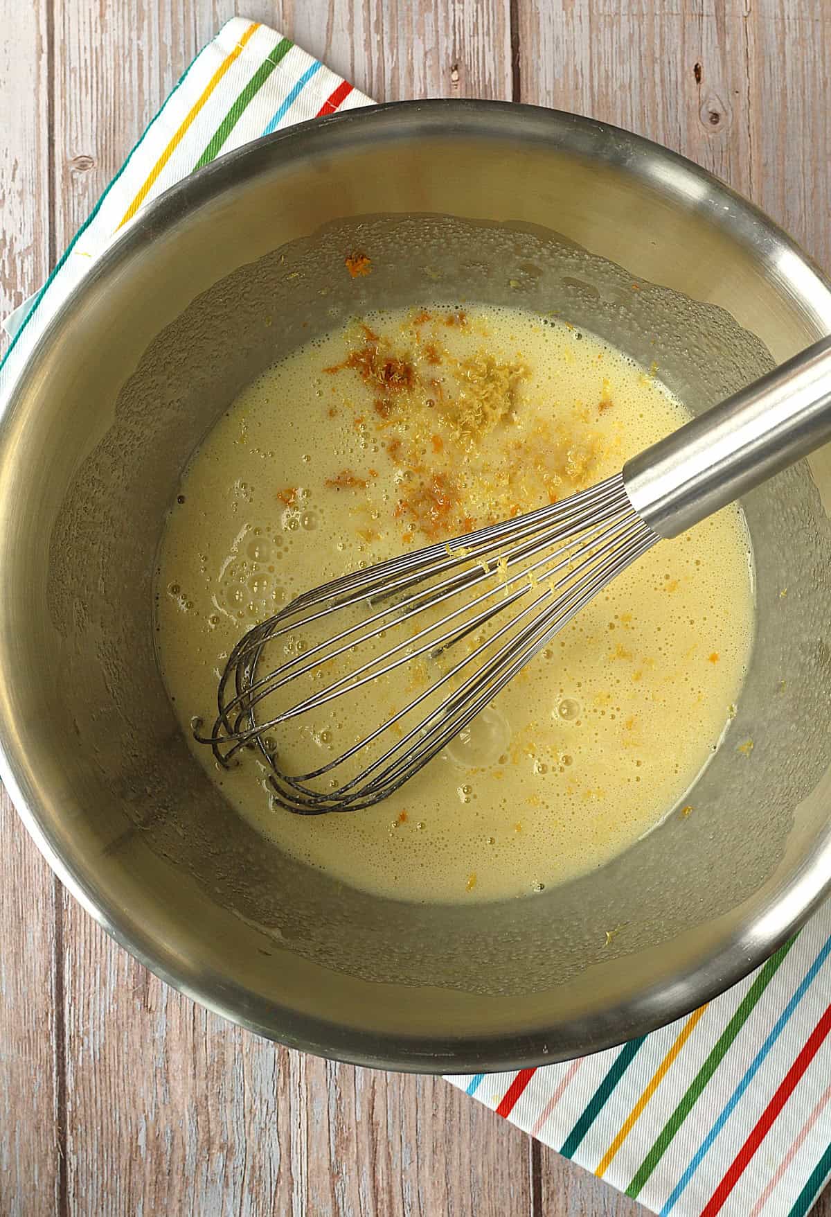 Orange and lemon zest added to bowl with wet ingredients for cupcakes and whisk.