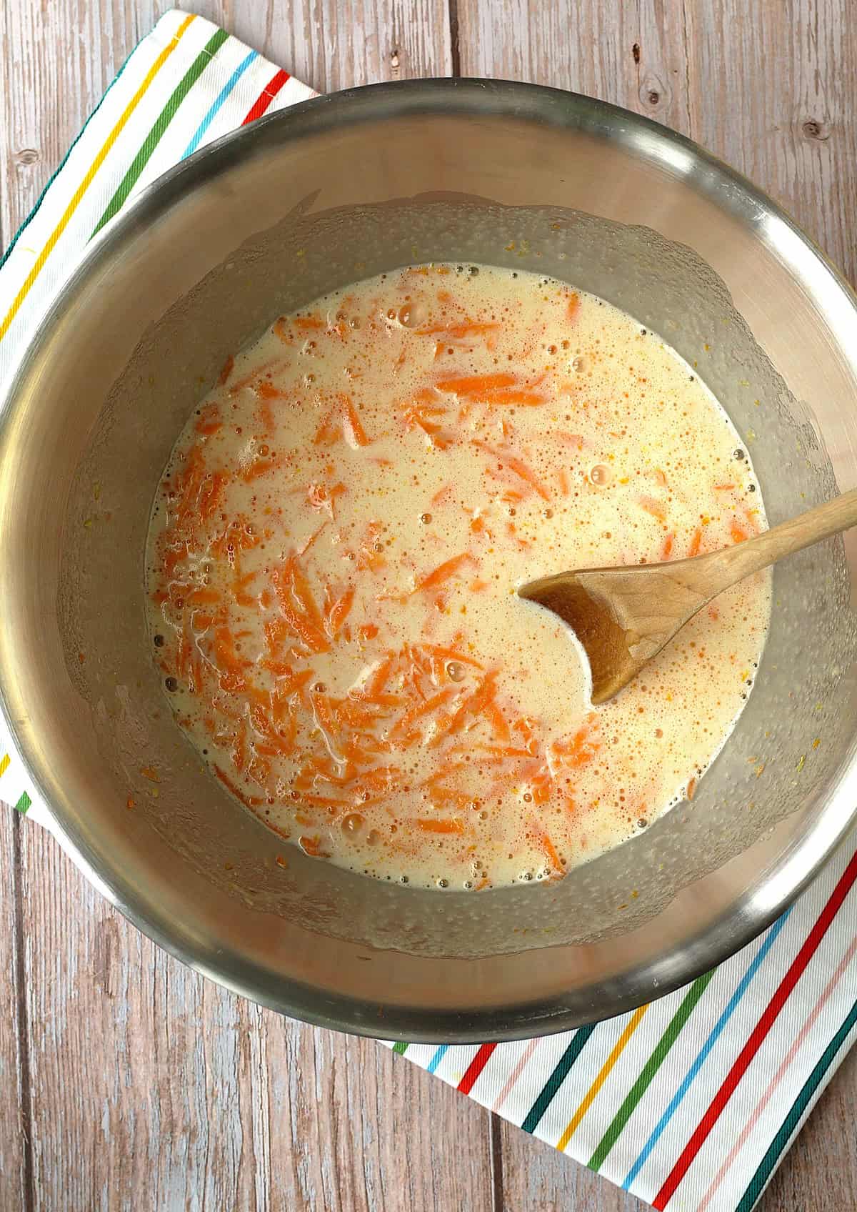 Grated carrots added to bowl with cupcake batter and wooden spoon.