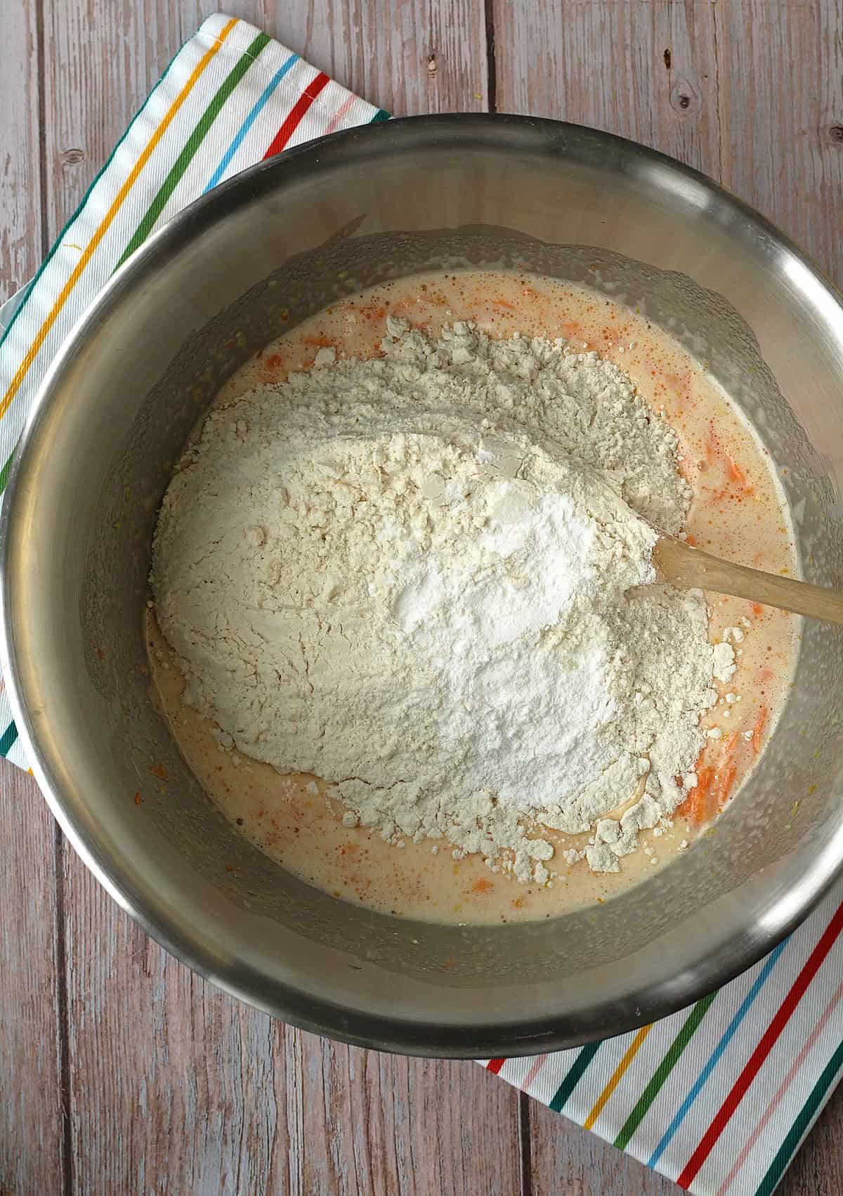 Dry ingredients added to metal bowl with wet ingredients for carrot cupcakes.