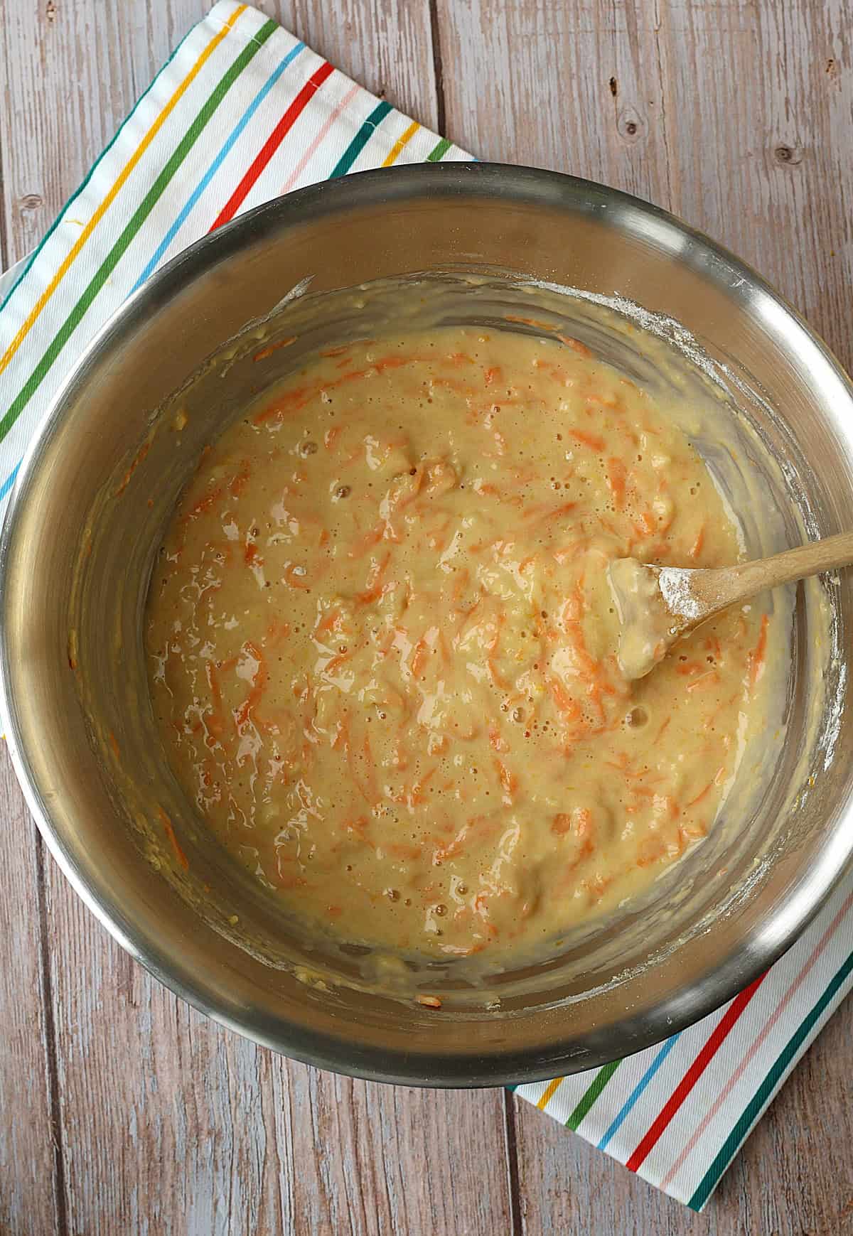 Orange, lemon and carrot cupcake batter in metal bowl with wooden spoon.
