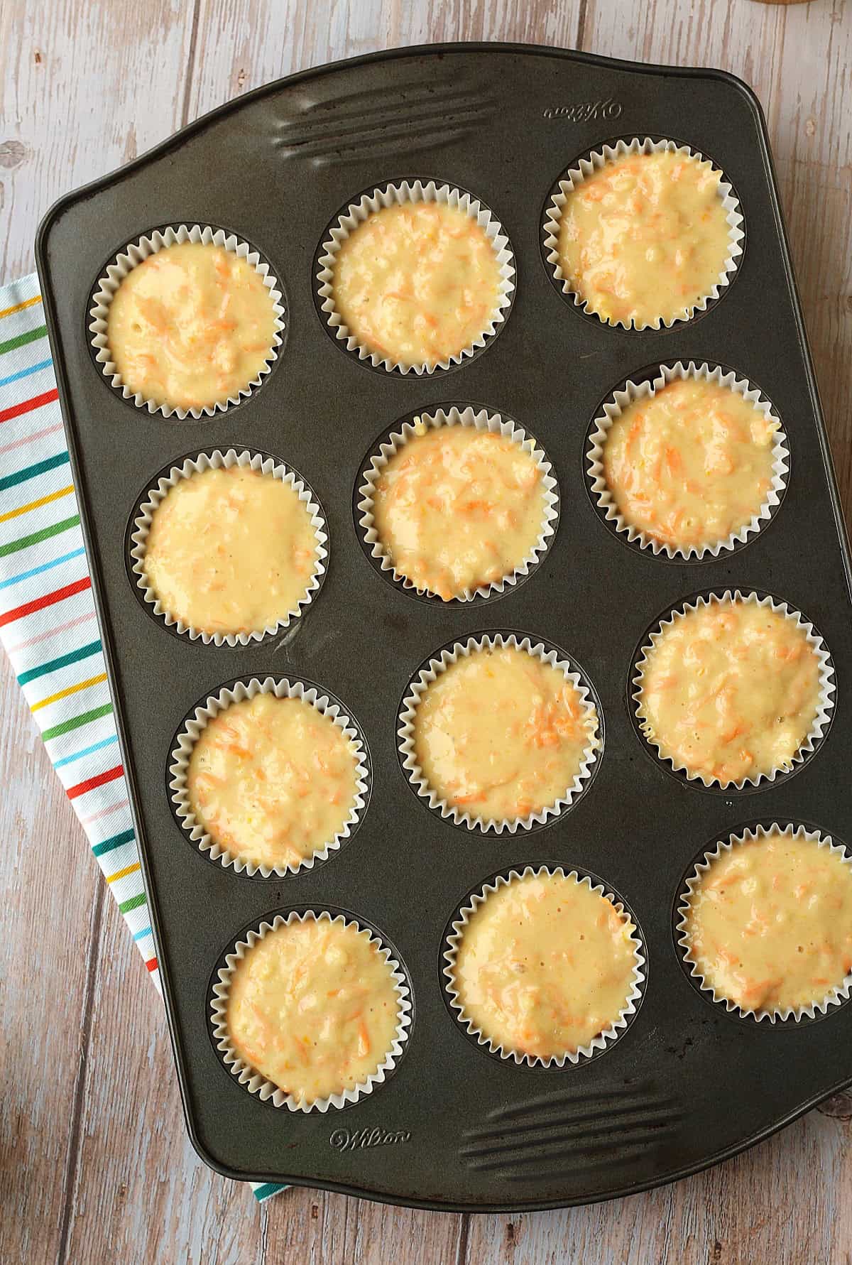Orange, lemon and carrot cupcake batter in muffin tin.