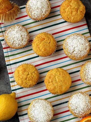 Citrus and carrot cupcakes on colorful dish cloth with orange and lemon wedges around them.