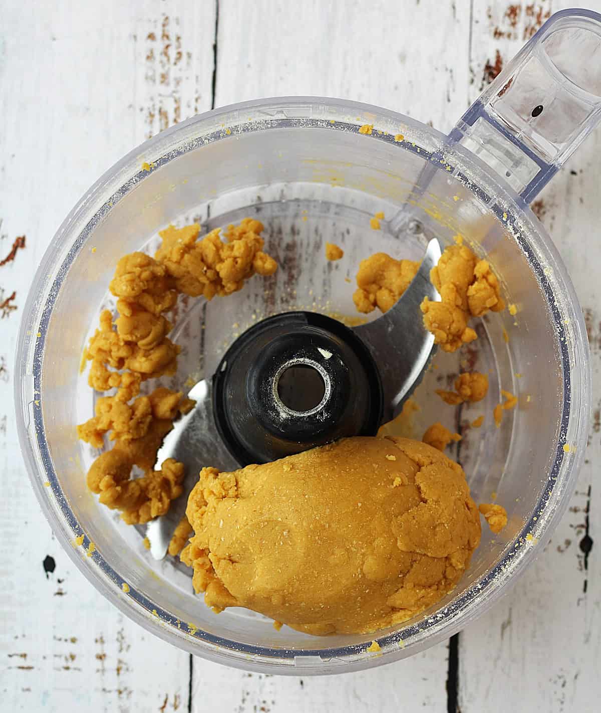 Chickpea flour tagliatelle dough wrapped around blade in food processor bowl.