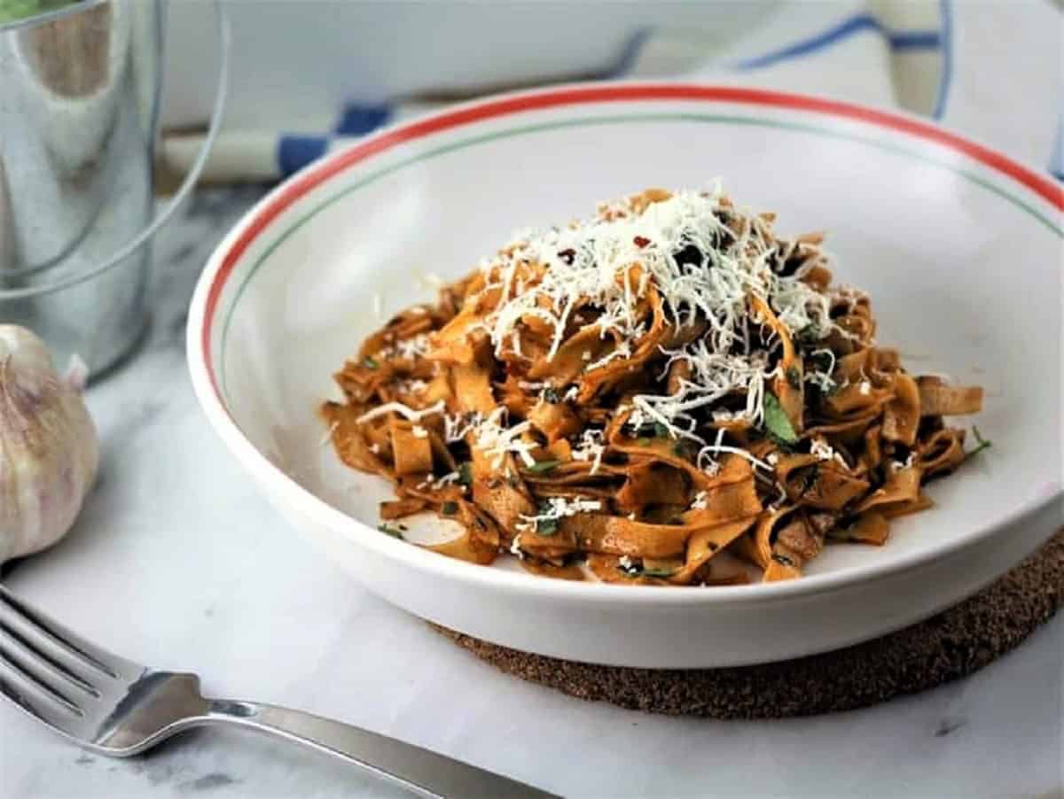 Bowl of chickpea flour tagliatelle with garlic paprika sauce topped with grated cheese.