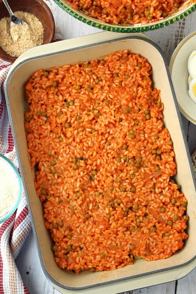 Rice with tomato sauce and peas layered on casserole dish for rice and eggplant timbale.