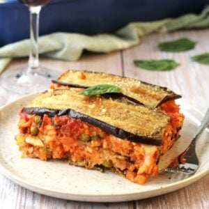 Rice and eggplant timballo layered dish on plate with wine glass behind it.