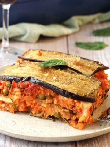 Rice and eggplant timballo layered dish on plate with wine glass behind it.