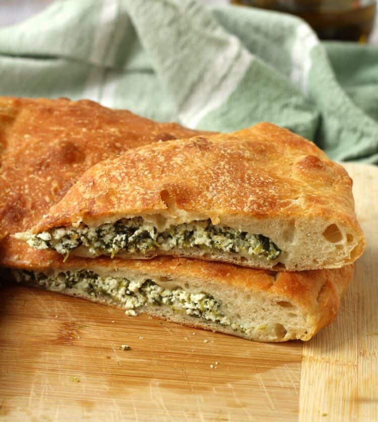 Spinach and ricotta scacciata bread cut into wedges on wood board.