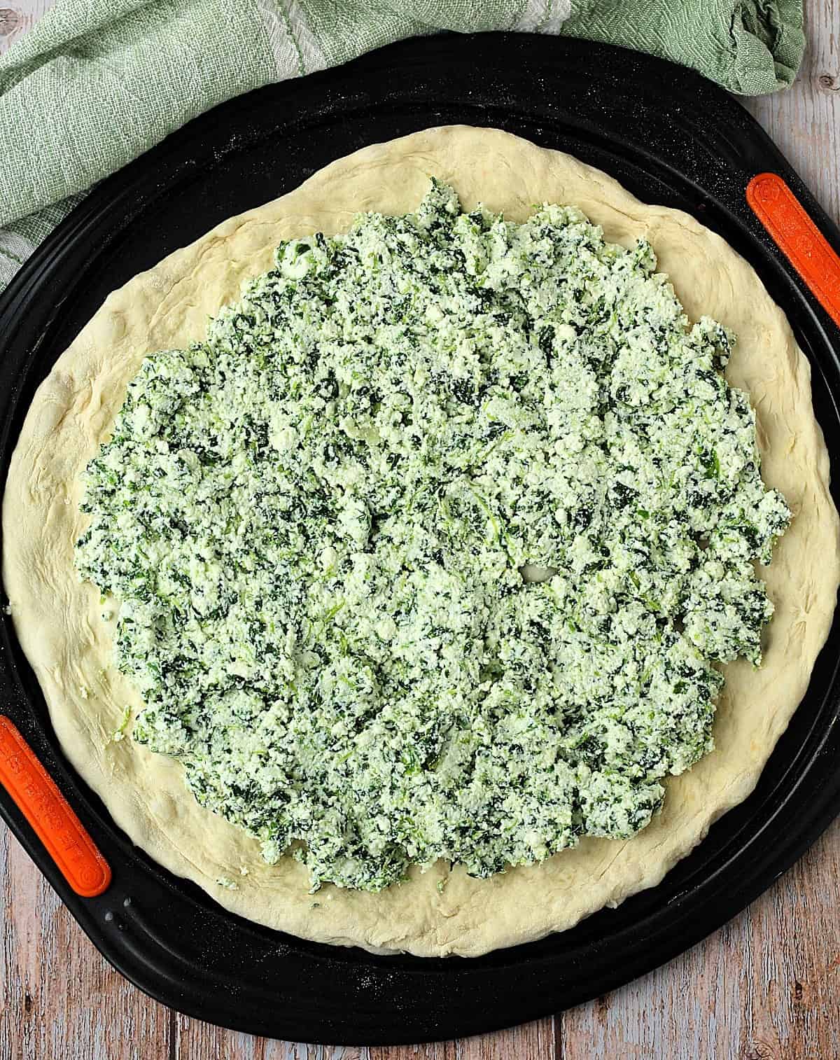 Flattened scacciata dough topped with spinach and ricotta.