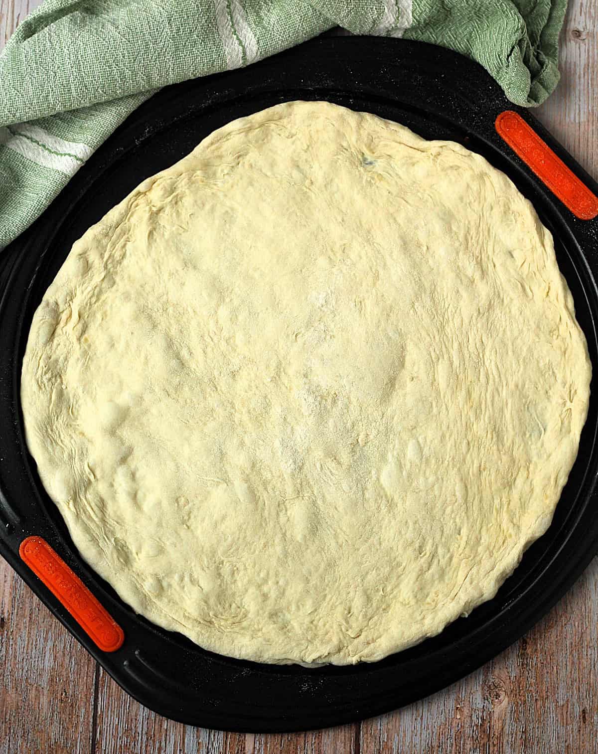Flattened pizza dough circle on pizza pan.