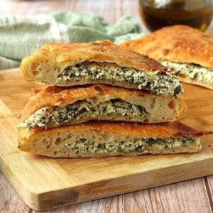 Spinach and ricotta filled scacciata bread cut into wedges and piled on wood board.