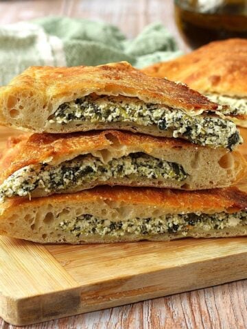Spinach and ricotta filled scacciata bread cut into wedges and piled on wood board.