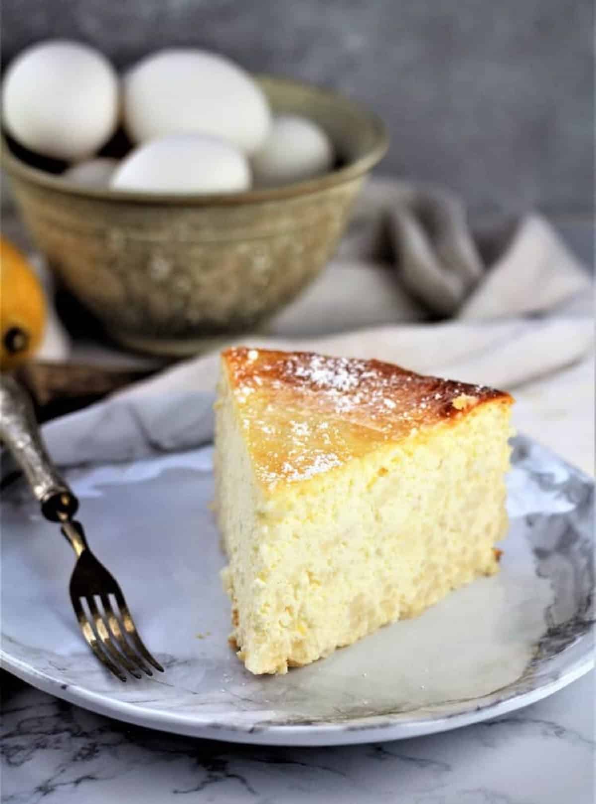 Slice of no crust pastiera on plate with fork and bowl of eggs behind it.