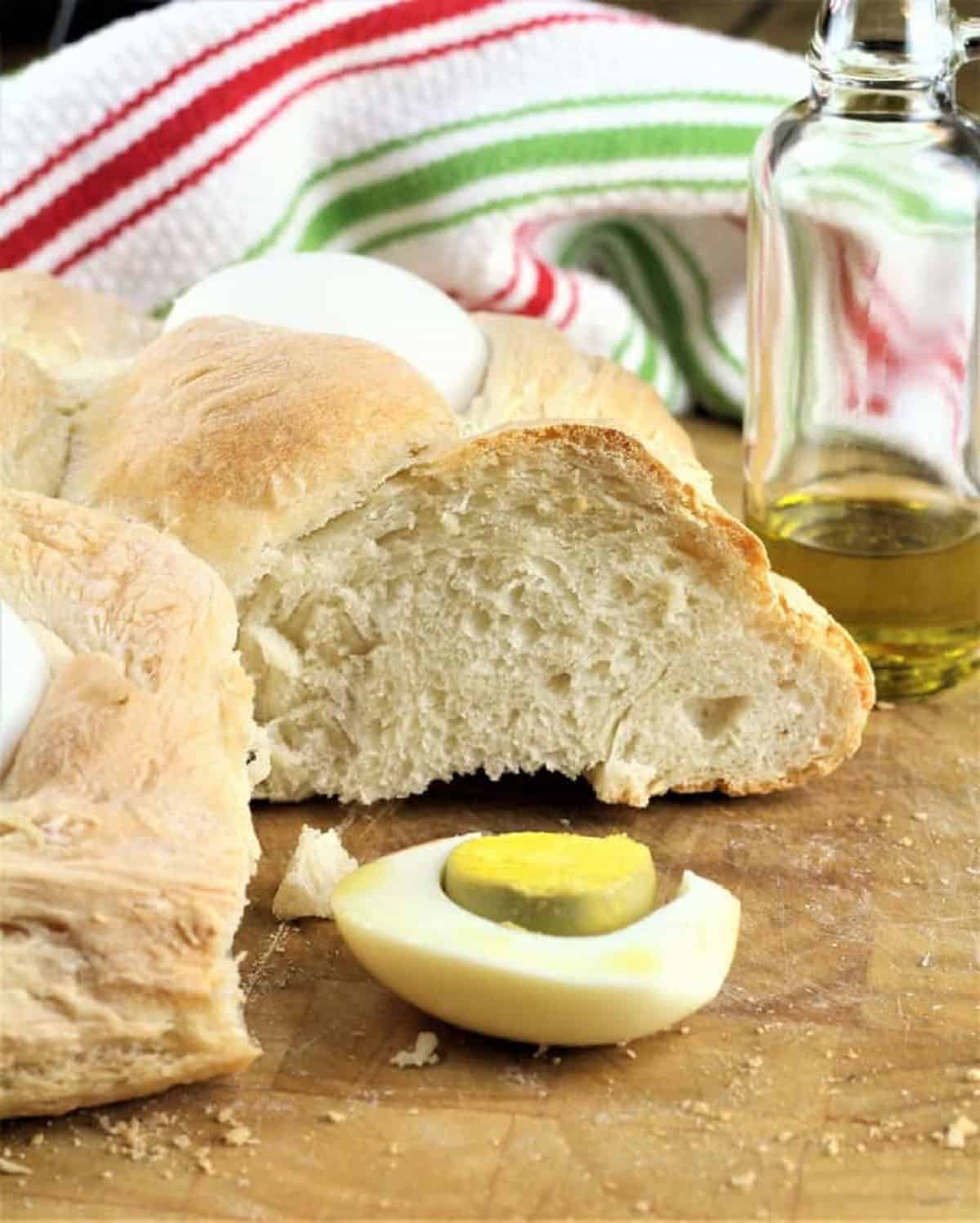 Sicilian Easter Bread (cuddura cu l'ova) Sicilian Easter bread cut open with sliced hard boiled egg and olive oil bottle next to it.
