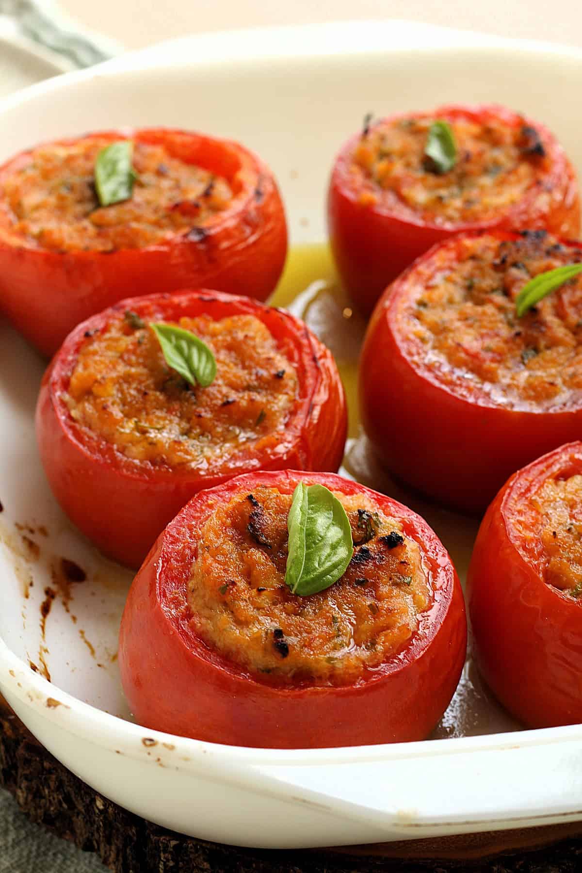 Baked stuffed tomatoes with breadcrumb filling in white casserole dish topped with fresh basil.