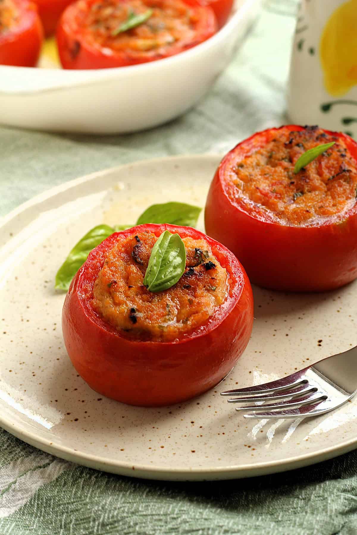 Two baked stuffed tomatoes with breadcrumbs on plate with fork.