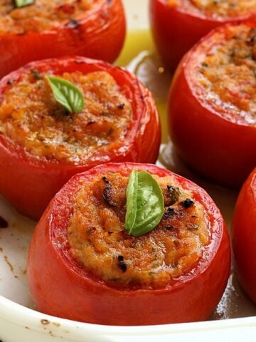 Baked stuffed tomatoes with breadcrumbs topped with basil in casserole dish.