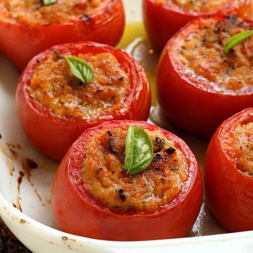 Baked stuffed tomatoes with breadcrumbs topped with basil in casserole dish.