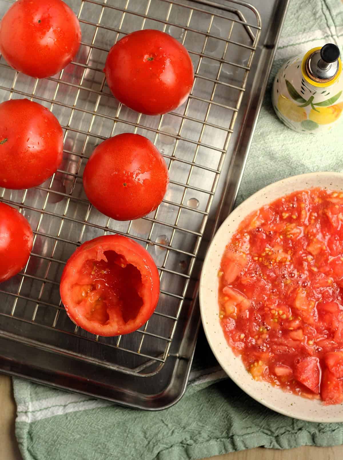 Hollowed tomatoes on wire rack next to bowl with tomato pulp for stuffed tomatoes.
