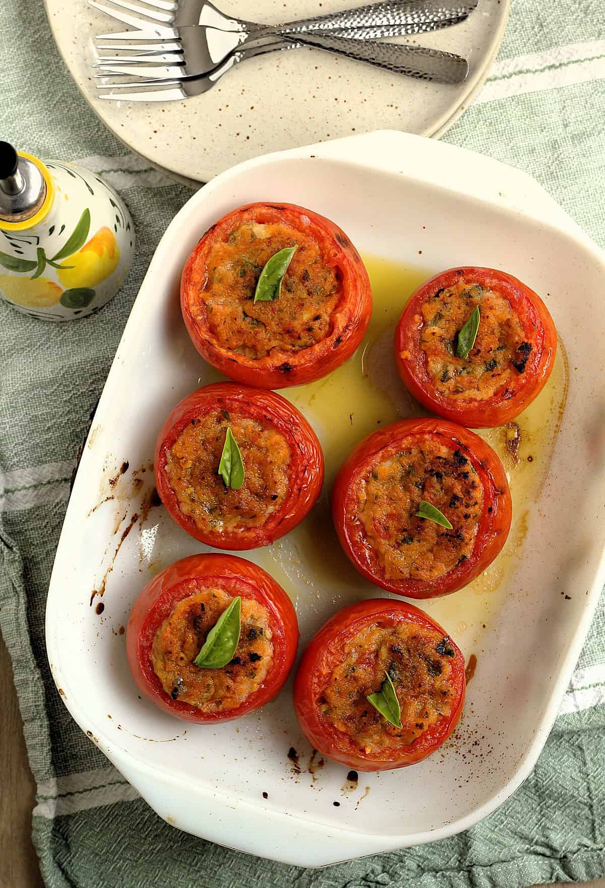 Italian baked stuffed tomatoes with breadcrumbs in casserole dish topped with basil leaf.