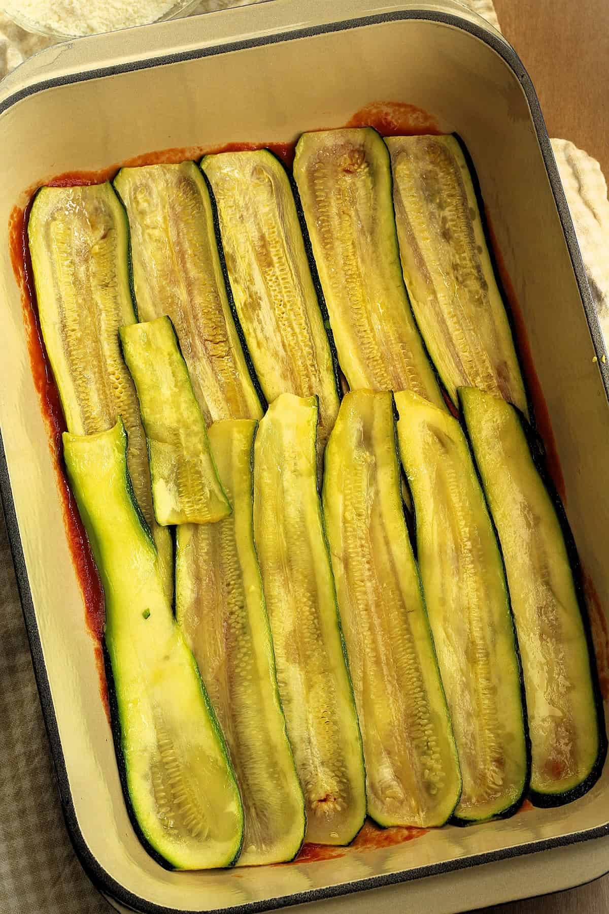 Sliced zucchini overlapping on baking casserole for parmigiana.