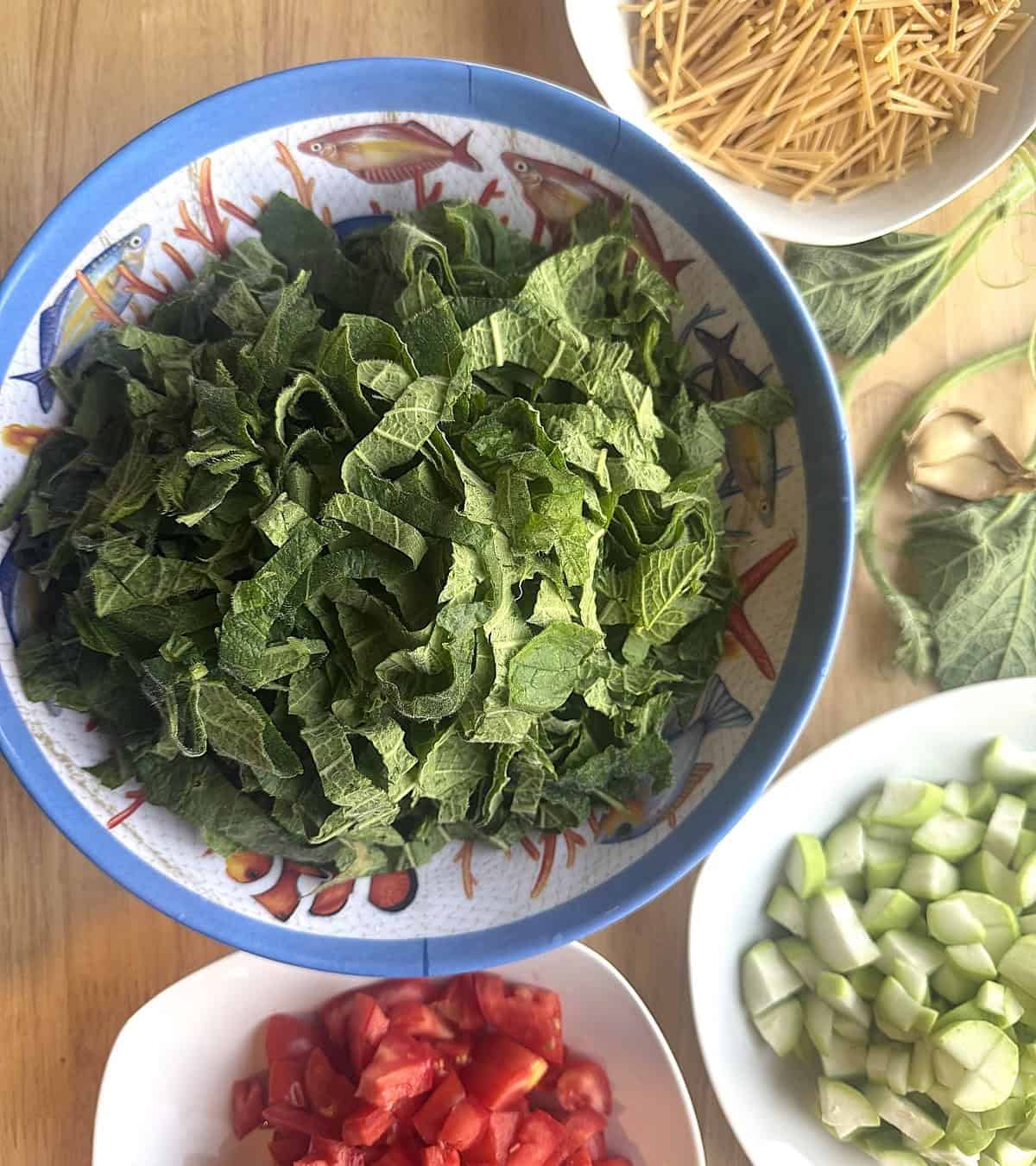 Bowls with chopped tenerumi; cucuzza; tomatoes and broken up spaghetti.