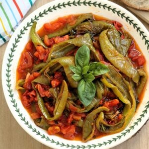 Italian fried peppers with tomatoes topped with basil in bowl.