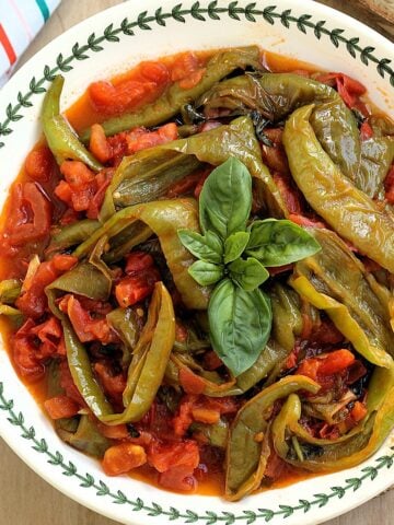 Italian fried peppers with tomatoes topped with basil in bowl.