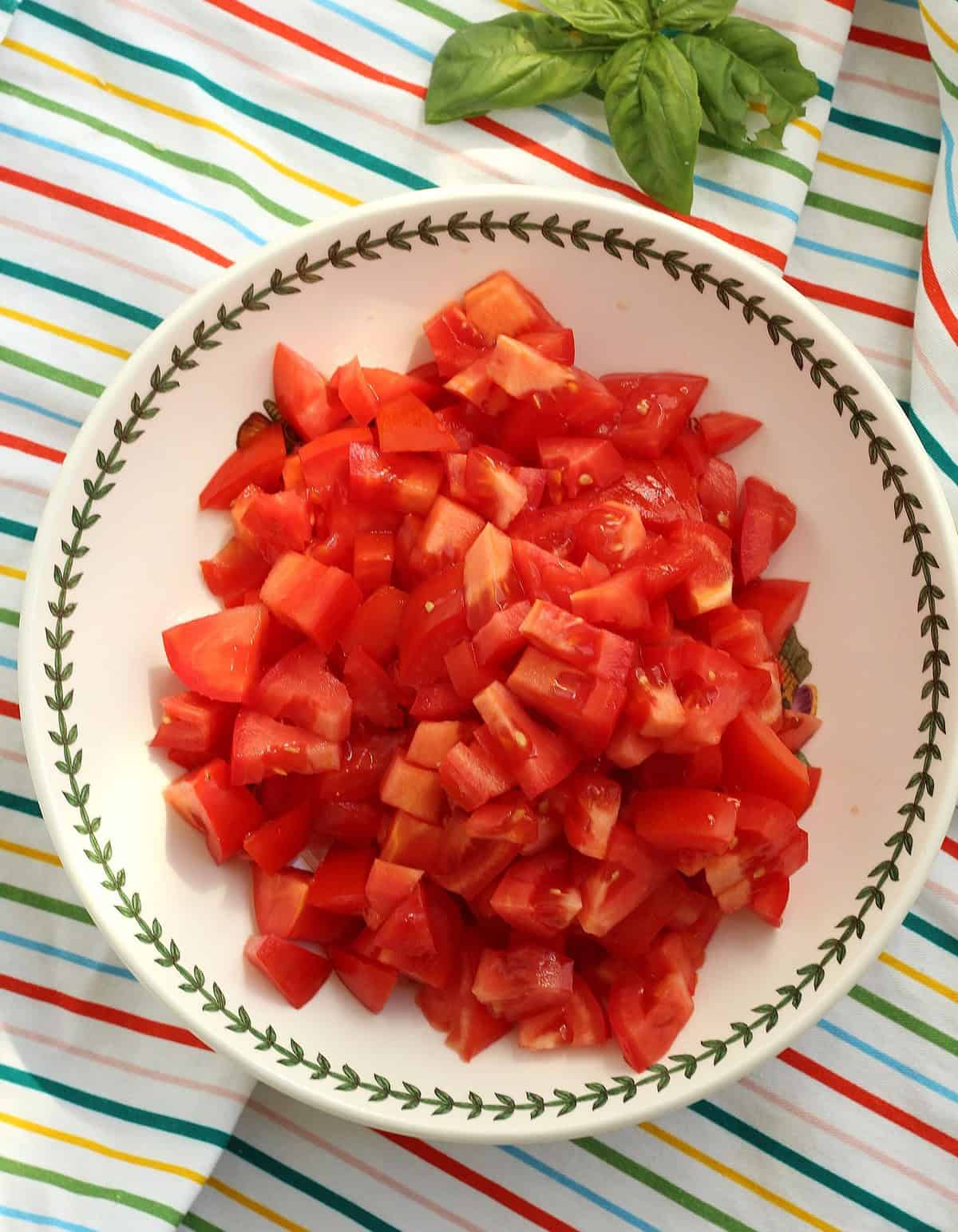 Diced tomatoes in bowl with fresh basil on the side.