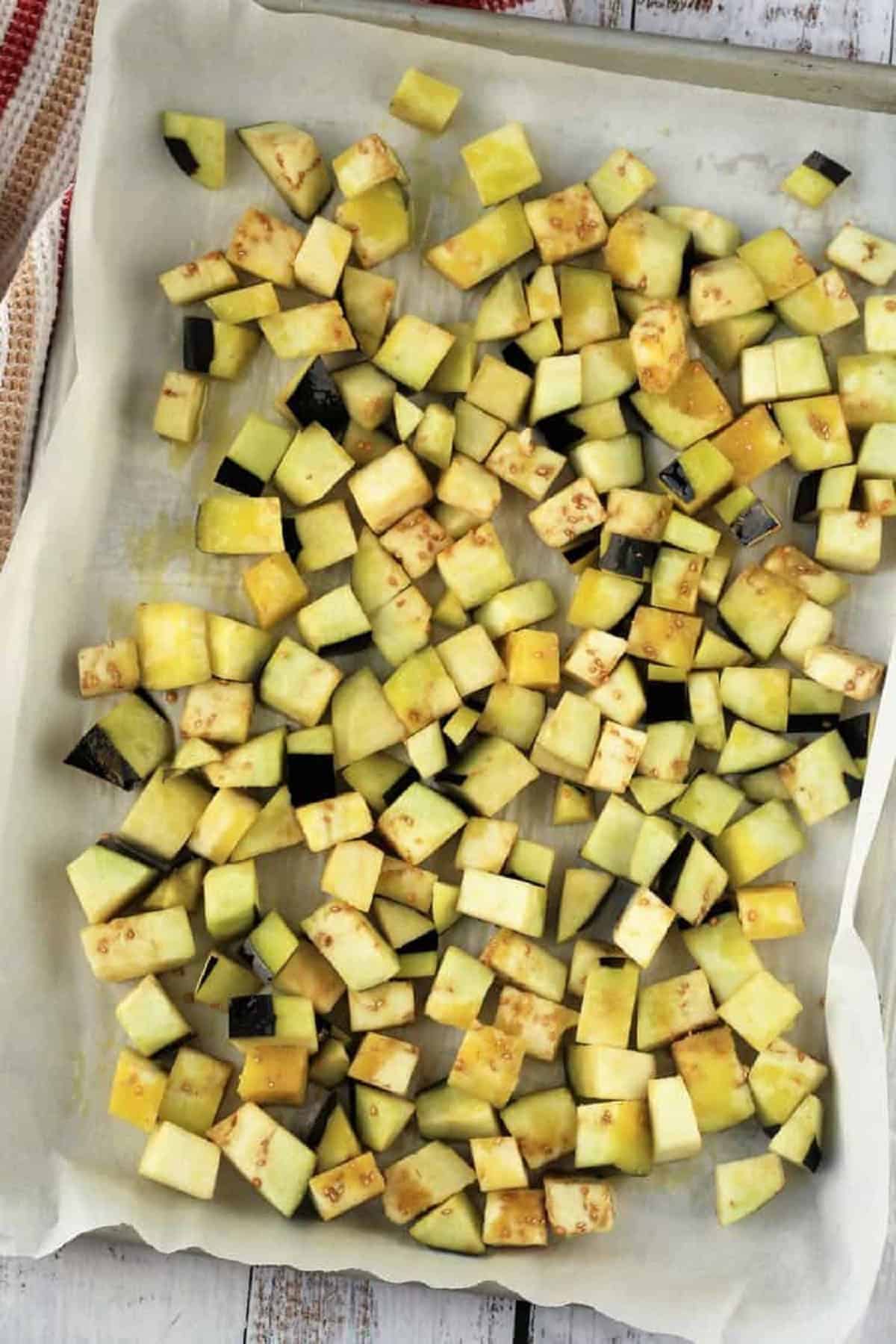 Eggplant cut into cubes tossed with olive oil on baking sheet for eggplant meatballs.