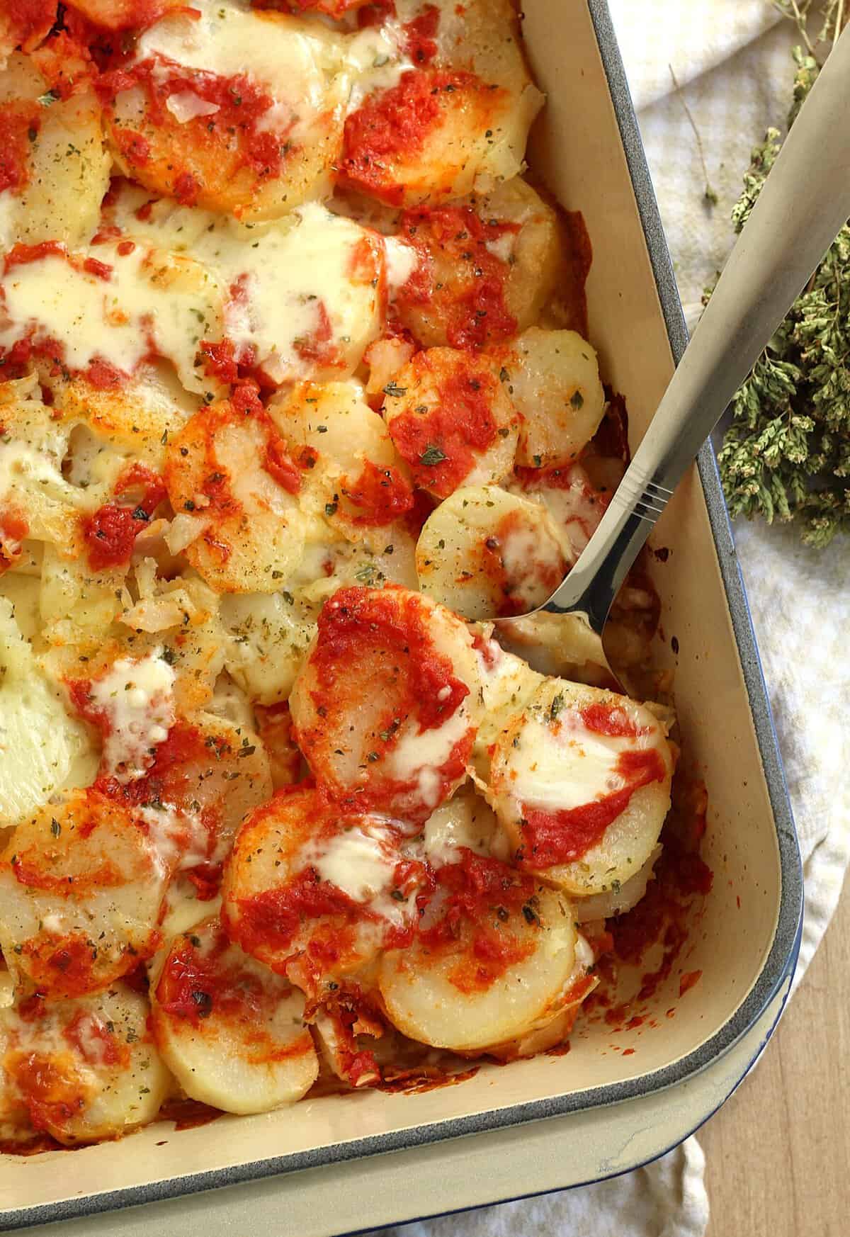 Patate alla pizzaiola with spatula serving a portion from casserole dish.