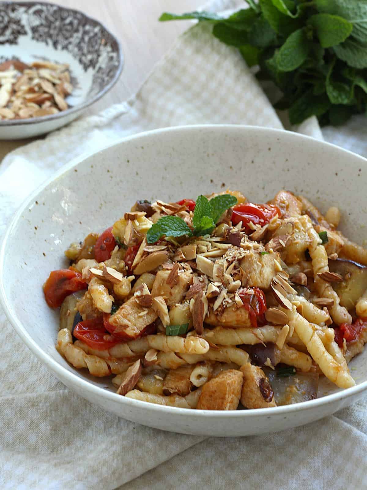 Swordfish pasta with eggplant, tomatoes, mint and almonds in bowl.