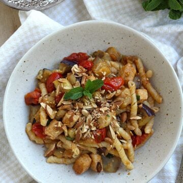 Pasta with eggplant, swordfish and tomatoes topped with mint and chopped almonds in a bowl.