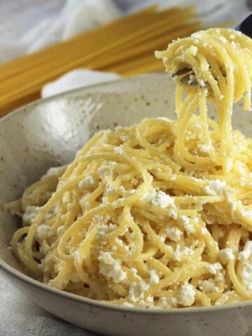 Pasta with ricotta in bowl twirled with fork.