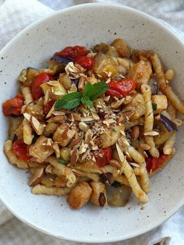 Pasta with eggplant, swordfish, tomatoes and mint topped with chopped almonds in bowl.