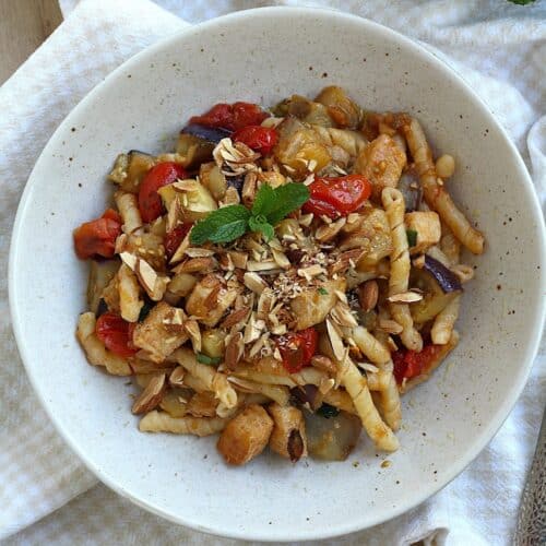 Pasta with eggplant, swordfish, tomatoes and mint topped with chopped almonds in bowl.