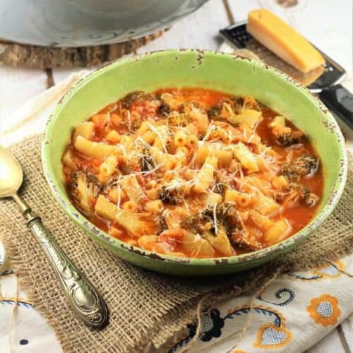 Broccoli soup with pasta in bowl topped with grated Parmigiano cheese.