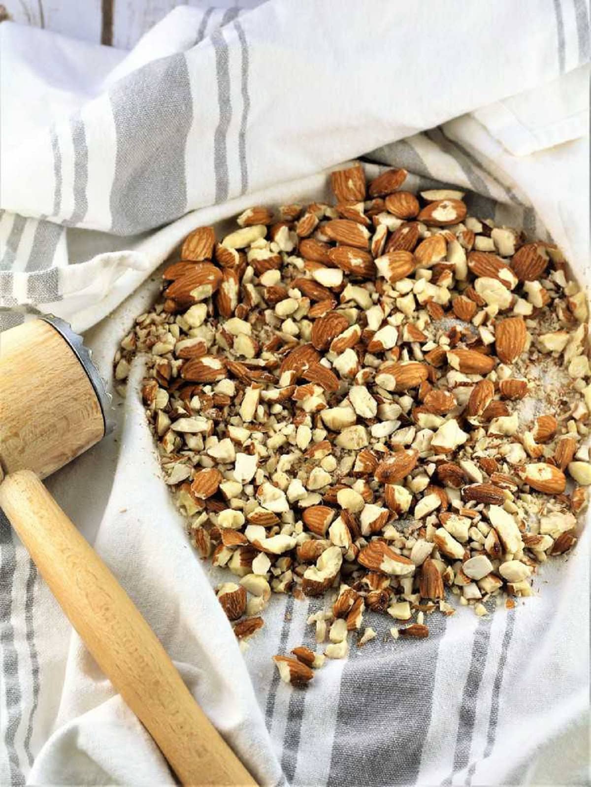 Chopped almonds on dish cloth with meat mallet for almond biscotti recipe.
