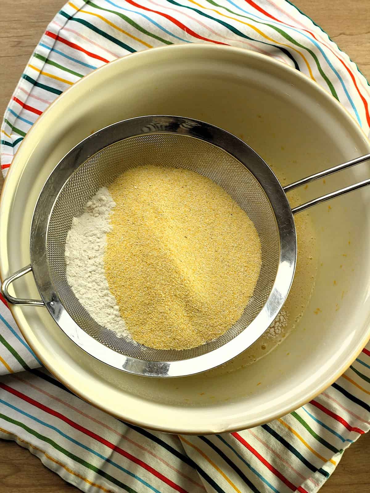Cornmeal, flour, baking powder and salt sifted into cornmeal biscotti wet ingredients in bowl.