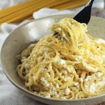 Pasta with ricotta in bowl twirled by fork.