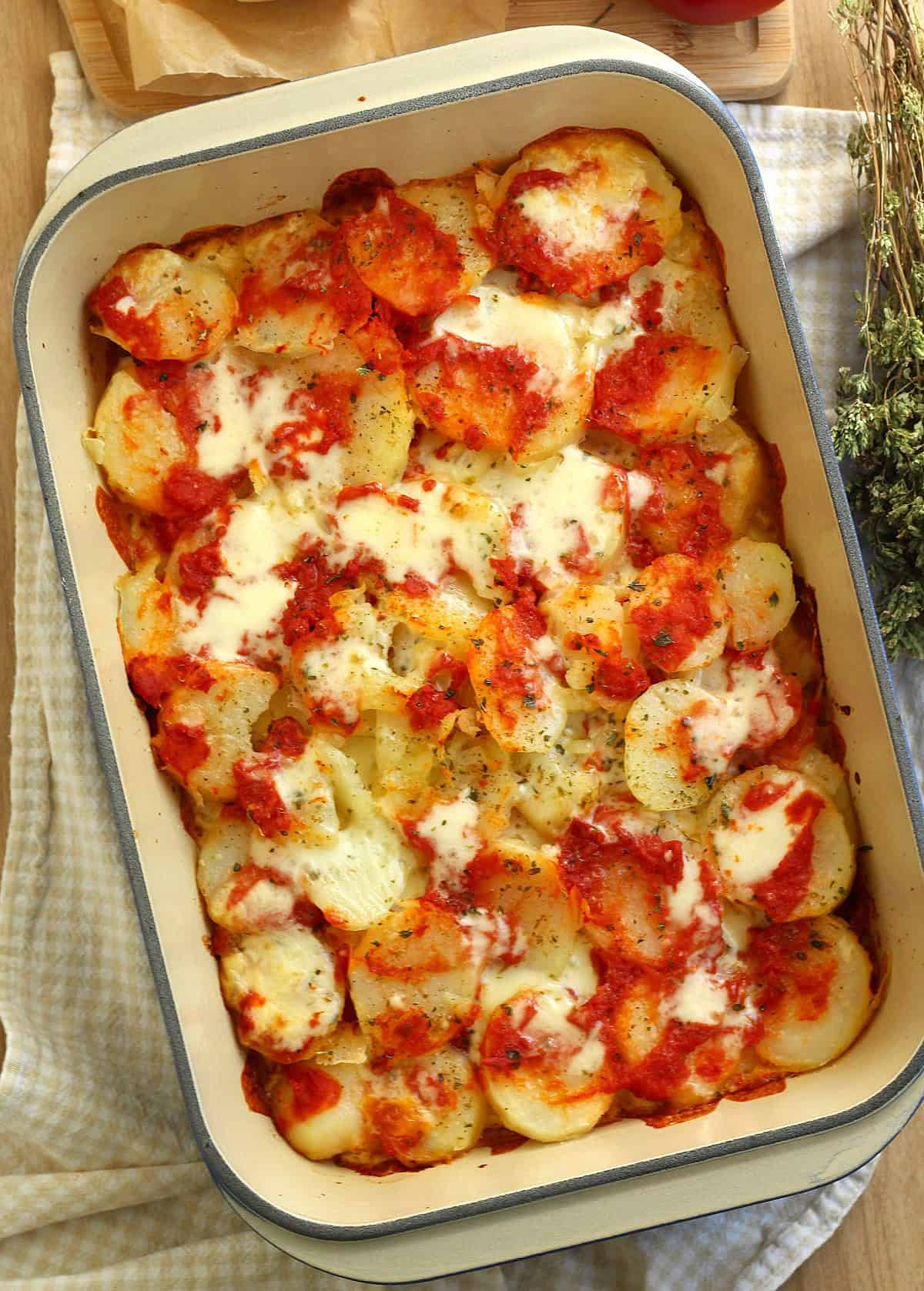 Potatoes pizzaiola topped with tomato sauce and mozzarella in casserole dish.