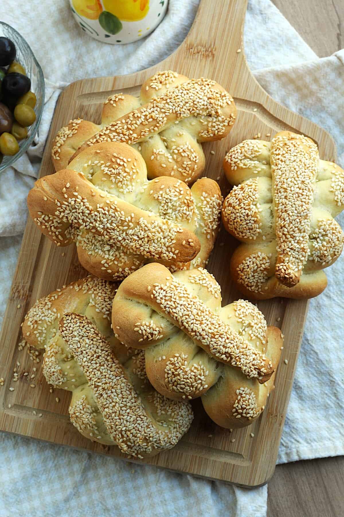 Sicilian Mafalda bread with sesame seeds piled on wood board.