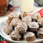 Sicilian chocolate spice cookies (tetù) piled on plate next to bottle of milk and coffee cup.