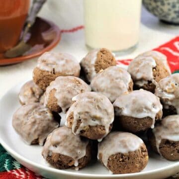 Sicilian chocolate spice cookies (tetù) piled on plate next to bottle of milk and coffee cup.